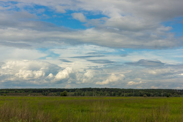 Obraz premium many cumulus white clouds in a bright blue summer sky over agricultural fields, landscape