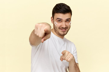 Signs, gestures, symbols and non verbal communication. Portrait of stylish confident young unshaven man with cream on cheeks pointing index fingers at camera and smiling, choosing you. Selective focus