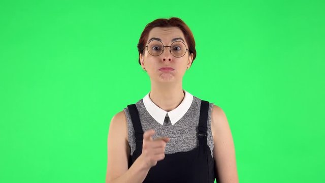 Portrait of funny girl is listening attentively and nodding his head pointing finger at viewer. Green screen