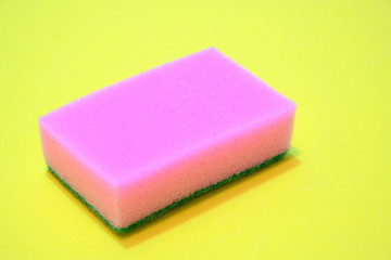 Pink sponge for washing dishes on a yellow background.