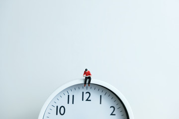 Miniature people for morning reading time concept - young man seating above clock reading a book