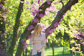 Young beautiful pregnant blonde. Stylish woman in the flowered park. Waiting for the baby