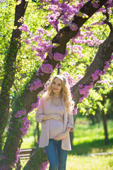 Young beautiful pregnant blonde. Stylish woman in the flowered park. Waiting for the baby