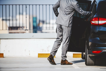 Cropped picture of sophisticated businessman in suit entering his modern and expensive car.
