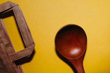 eco-friendly reusable tableware. Paper bag, wooden spoons on a smooth, clean yellow background, top view, flat ley. A poster for a reasonable consumption.