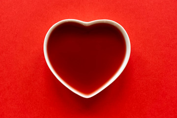 Valentine background. White porcelain heart filled with red liquid on a red background to be used as a template for valentine's day or wedding. Image with copy space.