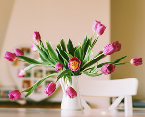 Beautiful bouquet of fresh purple tulips in jug placed on white table in living room