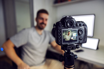 Young handsome bearded blogger filming himself at home office. He is talking about how to earn more money on stock market.