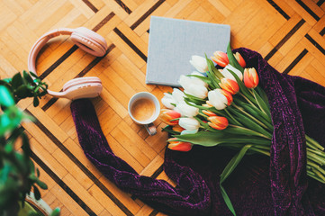 Spring still life, bouquet of tulips lying on purple pullover, small book with coffee cup and pink headphones