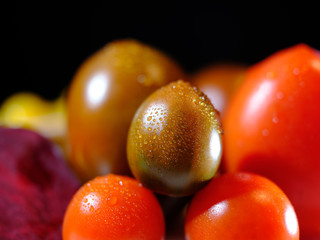close up of variants of tomatoes and raw beetroot, covered with fresh water drops, in front of a dark background