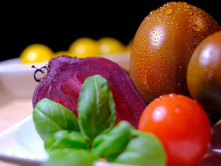 close up of variants of tomatoes and raw beetroot, covered with fresh water drops, on white tableware, in front of a dark background