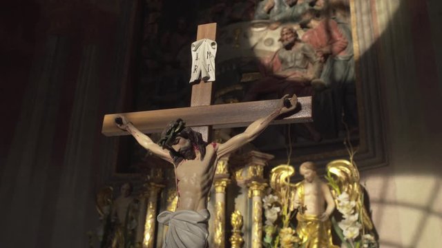 Religious sculpture of Jesus Christ Crucified on the Cross inside a dark church lit by direct sunshine