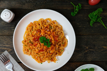 Spaghetti pasta with tomato sauce and parsley in white dish on black wooden table.