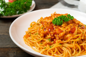 Spaghetti pasta with tomato sauce and parsley in white dish on black wooden table.