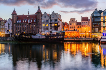 Fototapeta na wymiar Sightseeing of Poland. Cityscape of Gdansk in the night. Facades of buildings and a ship on the motlava river with illumination