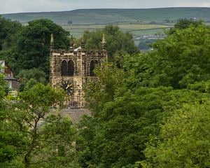 The clock tower of Bingley's ancient All Saints Parish Church glimpsed through the trees with the moorland hills in the distance