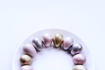 Colored painted pearl chicken and quail eggs of pink, silver, golden color on a purple plate pastel background. Minimalistic creative idea easter festive flat lay. Copyspace for text