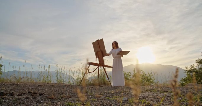 Multiethnic girl enjoying her hobby in mountains, creating an art piece on easel inspired by view - recreational pursuit, inspirational landscape concept 4k footage