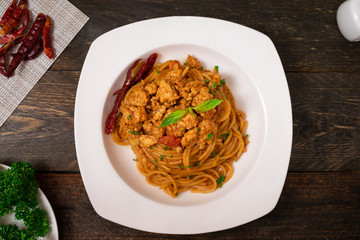 Spicy spaghetti pasta with fried chicken and chili in white dish on black wooden table.