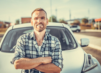 An attractive young man stands near a white car. Toned photo.