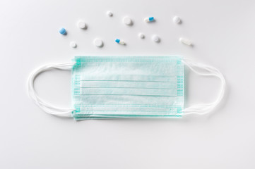 Medical surgical masks and pharmaceutical pills over light gray background.