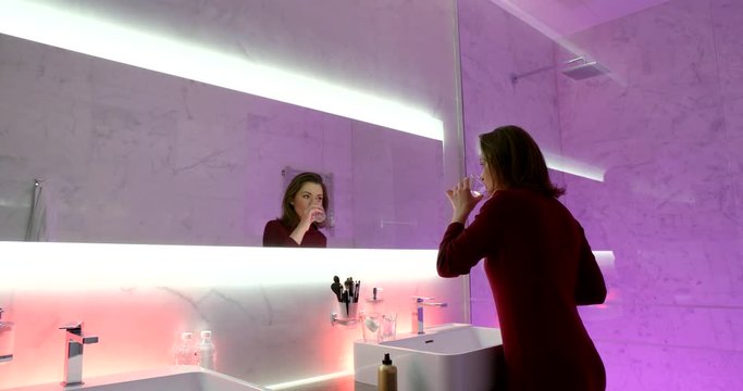 adult brunette woman is cleaning teeth in bathroom of luxury hotel in morning