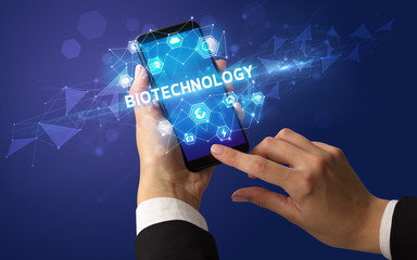 Female hand holding smartphone with BIOTECHNOLOGY inscription, modern technology concept