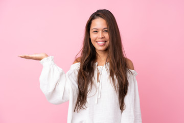 Young Brazilian girl over isolated pink background holding copyspace imaginary on the palm to insert an ad