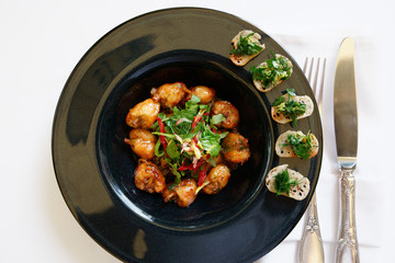 Fried frog legs in black plate on restaurant table, French dish