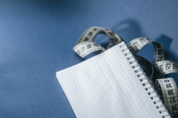 Flat lay notepad with measuring tape on classic blue background. Diet before summer. Tailoring equipment
