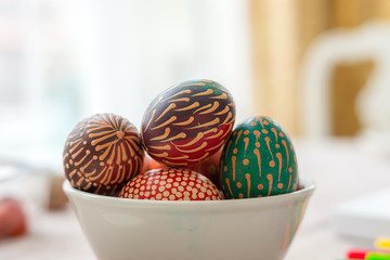 Colourful wax painted Easter eggs in bowl on wooden table, wax painted ornaments, rainbow flowers, dots