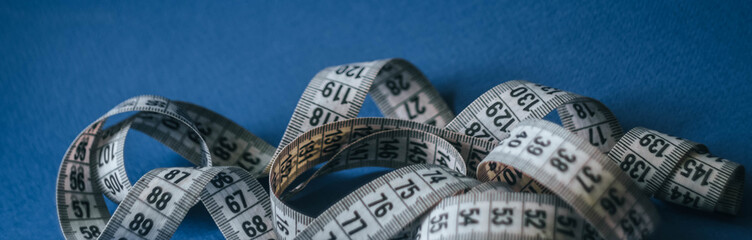 Measuring tape on classic blue background. Tailoring concept. Diet wallpaper. 