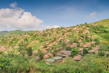 view of many huts on side hill around with green trees and cloudy sky background, refugee camp,...