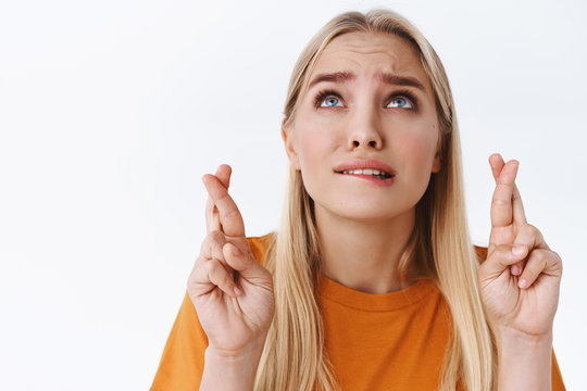Close-up worried, very nervous blond caucasian woman in orange t-shirt, fingers crossed hope god hear prayers as furrow eyebrows intense, anxiously supplicating, stand white background
