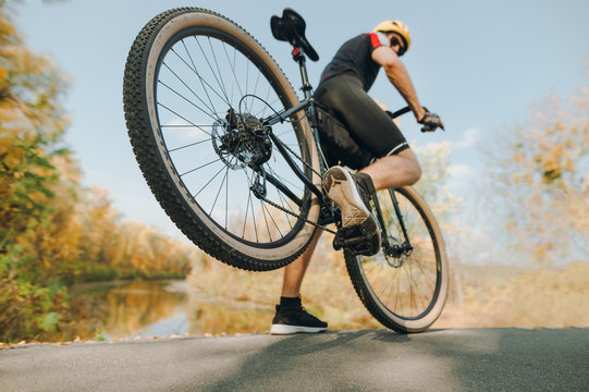 Action photo of a cyclist doing the trick in the park, lifting the rear wheel up. A man is extreme riding on the road in the park. Closeup photo of an extreme cyclist
