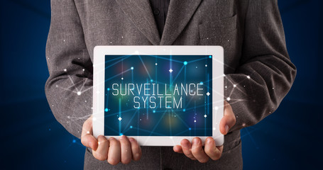 Young business person working on tablet and shows the digital sign: SURVEILLANCE SYSTEM