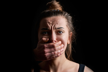 Stressed unhappy scared crying woman victim in fear with closed mouth on a dark black background...
