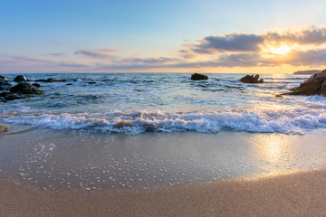 sunrise on the beach. beautiful summer scenery. rocks on the sand. calm waves on the water. clouds on the sky. wide panoramic view