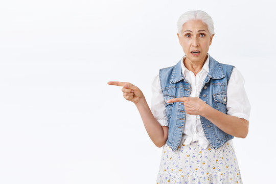 Doubtful, Skeptical, Indecisive Senior Woman, Grey Hair, Wear Denim Vest, Dress, Pointing Left And Look Camera Hesitant, Unsure, Asking Question, Advice, Consulting With Daughter, White Background