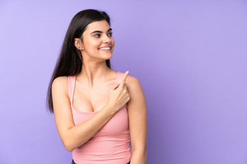 Young woman over isolated purple background surprised and pointing side