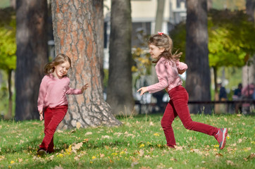 Two little sisters has fun outdoors in the park on a warm autumn day. The concept of a happy carefree childhood.