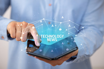 Businessman holding a foldable smartphone with TECHNOLOGY NEWS inscription, new technology concept