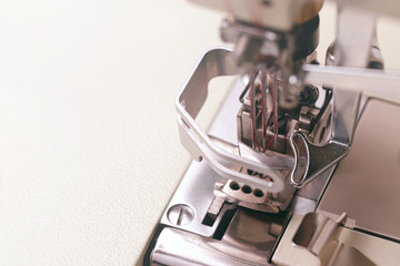 close up on the working area of a solid industrial coverlock sewing machine with three needles and red thread - background blanked out blurry