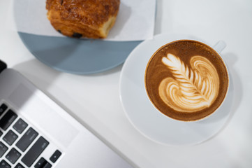 Close up of Latte art coffee cup with keyboard of laptop computer
