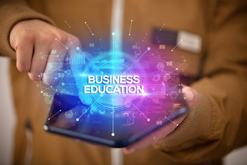 Businessman holding a foldable smartphone with BUSINESS EDUCATION inscription, new business concept