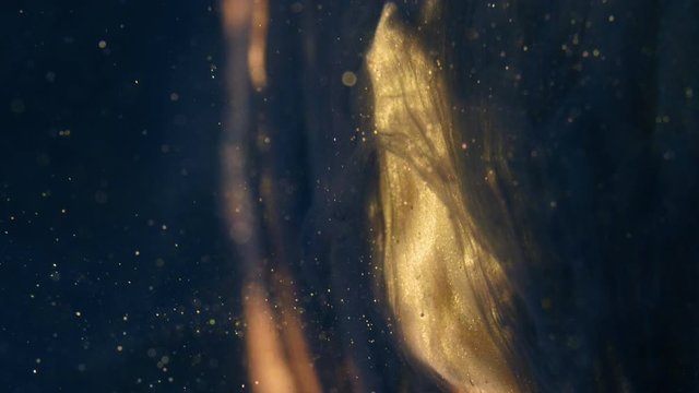 Golden ink particles flows in water as colorful chaos on the black background