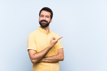 Young man with beard over isolated blue background pointing to the side to present a product