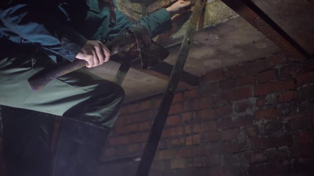 a man with an ax and rubber boots, descends the iron stairs to the basement of red brick in stamp.
