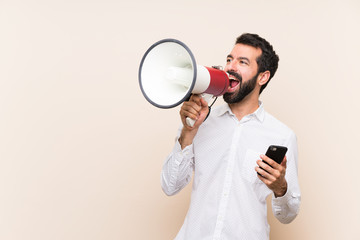 Young man with beard holding a mobile shouting through a megaphone