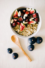 a plate of healthy Breakfast with oatmeal, figs and cashew nuts on a white table with a bamboo spoon. vegan food